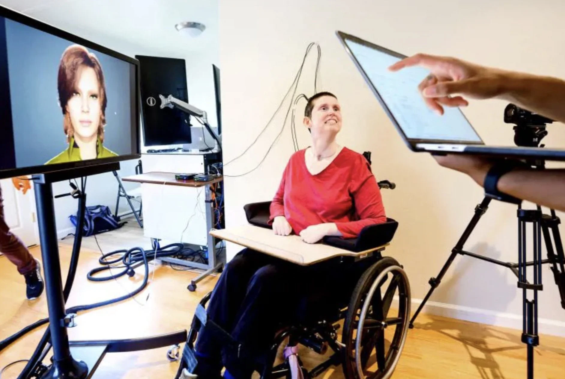 A research participant in a wheelchair watches a screen showing a digital avatar during a brain-computer interface session.